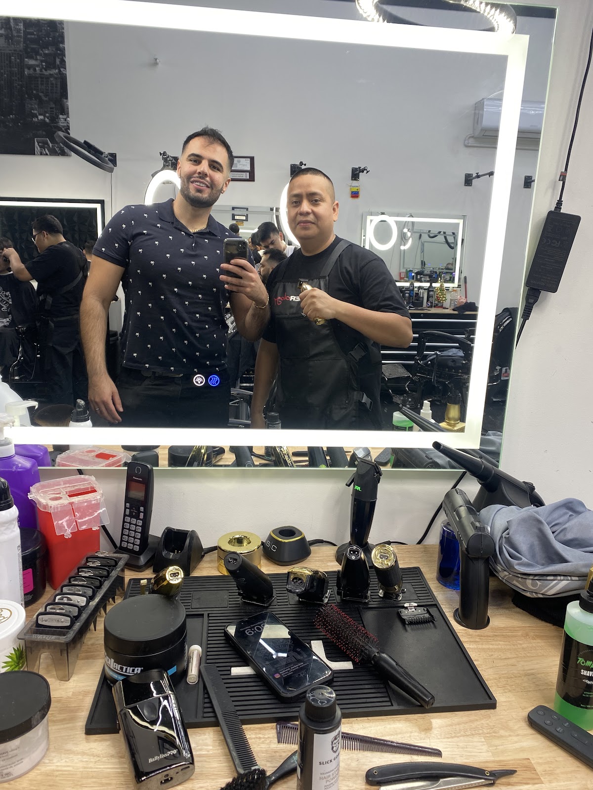 A barber and client in the mirror above a bench of clippers