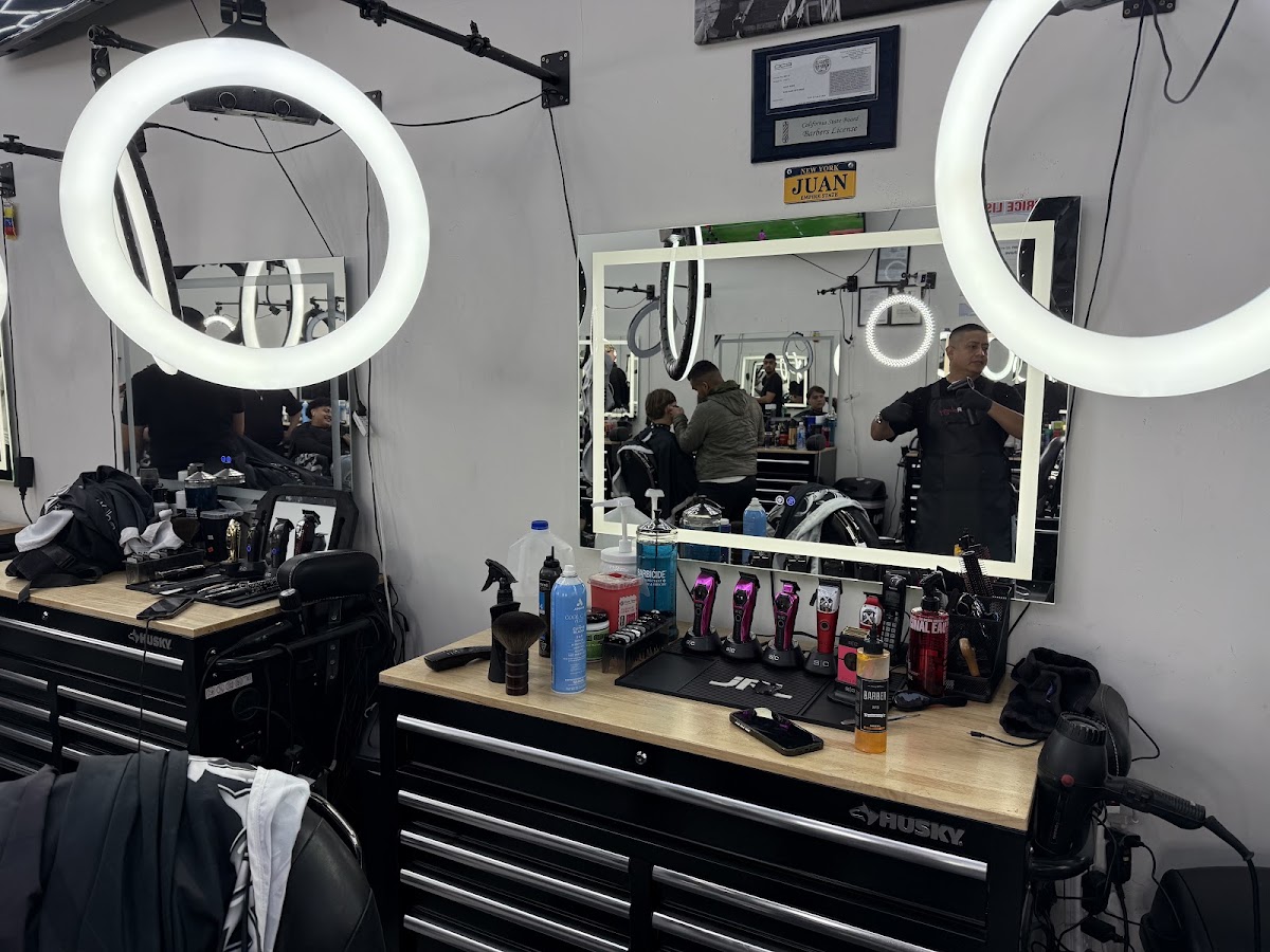 A barber station with ring lights, clippers laid out and the California State Board barber license framed on the wall