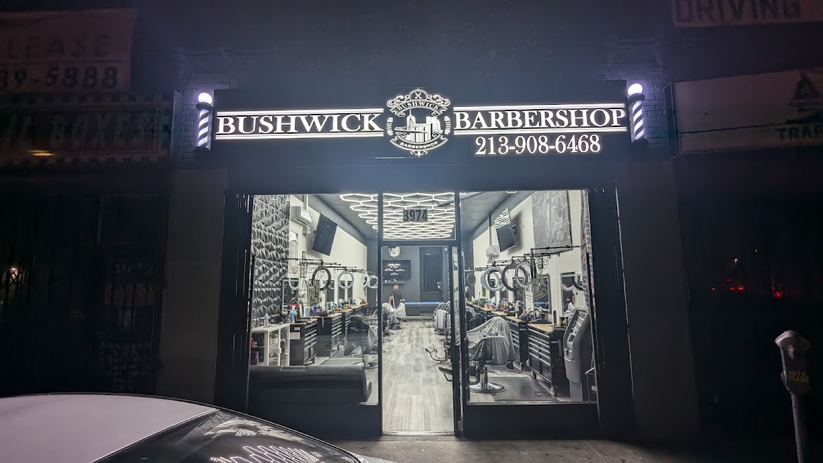 The illuminated Bushwick Barbershop sign and lit barber poles at night